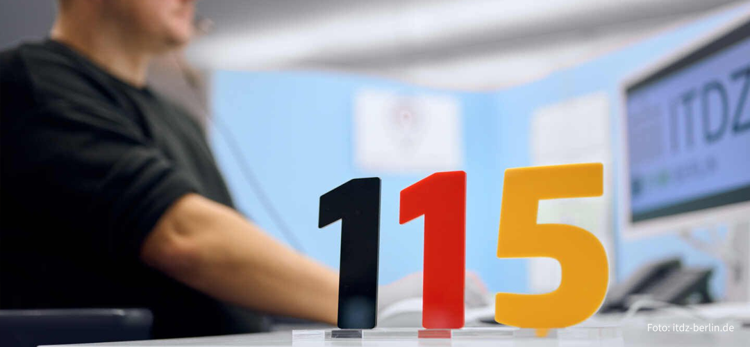 Behördennummer 115 als Aufsteller auf einem Schreibtisch im Call-Center