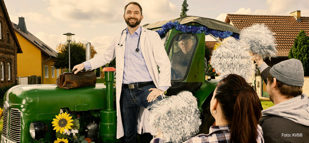 Dorfbewohner mit Pompoms jubeln einem Arzt zu, der auf einem Traktor steht