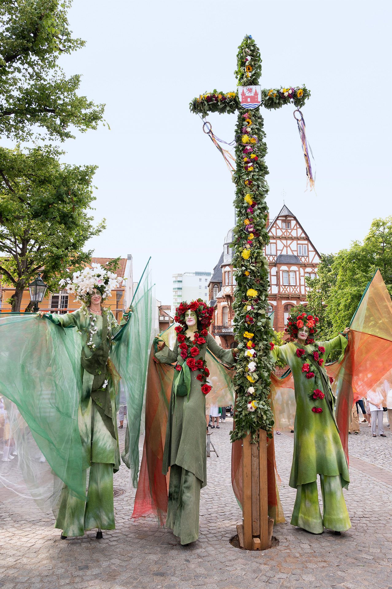 Foto: 3 Stelzenläuferinnen in blumigen Kostümen an der Mittsommerstange Foto: 3 Stelzenläuferinnen in blumigen Kostümen an der Mittsommerstange