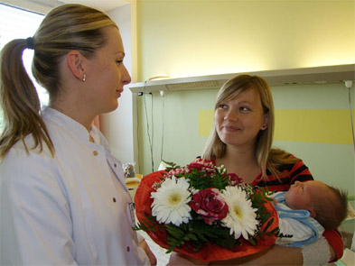 Foto: Ärztin überreicht Blumenstrauß an Mutter mit Baby Foto: Ärztin überreicht Blumenstrauß an Mutter mit Baby