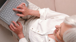Foto: Seniorin mit einem Laptop auf den Knien Foto: Seniorin mit einem Laptop auf den Knien