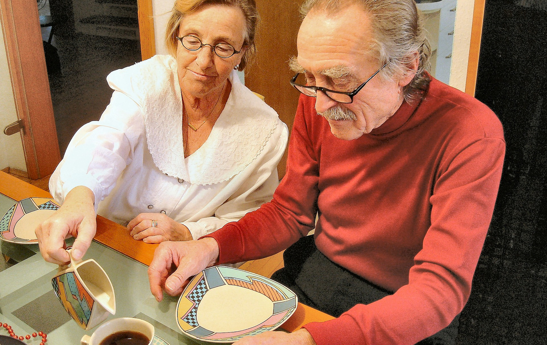 Foto: Frau gießt einem alten Mann Milch in den Kaffee Foto: Frau gießt einem alten Mann Milch in den Kaffee