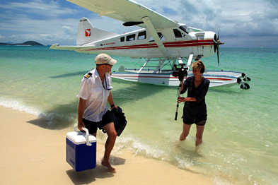 Foto: Filmerin steht im Wasser und filmt den Piloten eines Wasserflugzeugs am Strand Foto: Filmerin steht im Wasser und filmt den Piloten eines Wasserflugzeugs am Strand