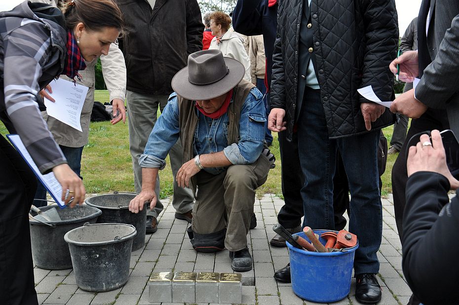 Mann kniet auf Straßenfalster vor vier Stolpersteinen mit Messingplatten