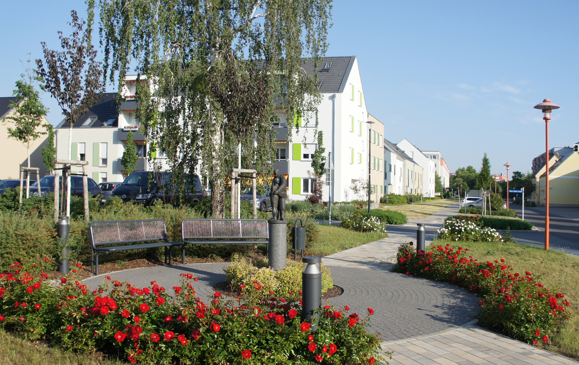 Foto: neue Wohnhäusern mit Bänken, Rosenrabatten und Skulptur im Vordergrund