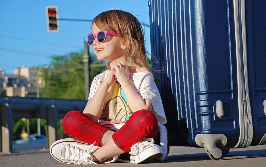 Foto: Mädchen mit Sonnenbrille lehnt an einem Rollkoffer Foto: Mädchen mit Sonnenbrille lehnt an einem Rollkoffer