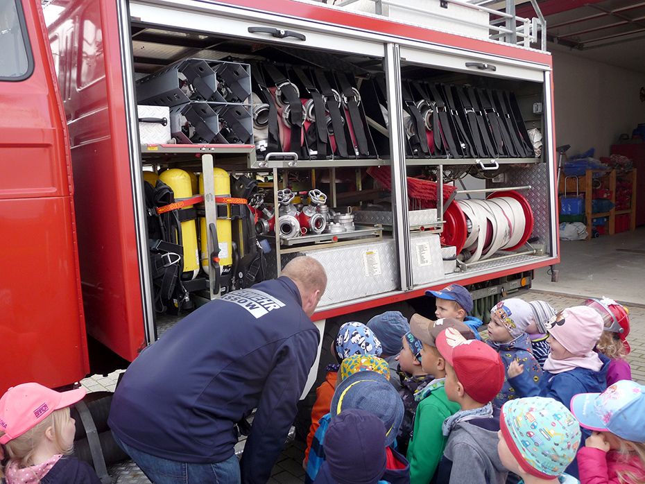 Foto: Feuerwehrmann zeigt der Kindergruppe ein Feuerwehrauto