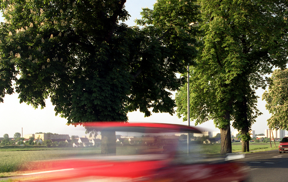 Foto: Rotes Auto fährt rasant vorbei. Foto: Rotes Auto fährt rasant vorbei.