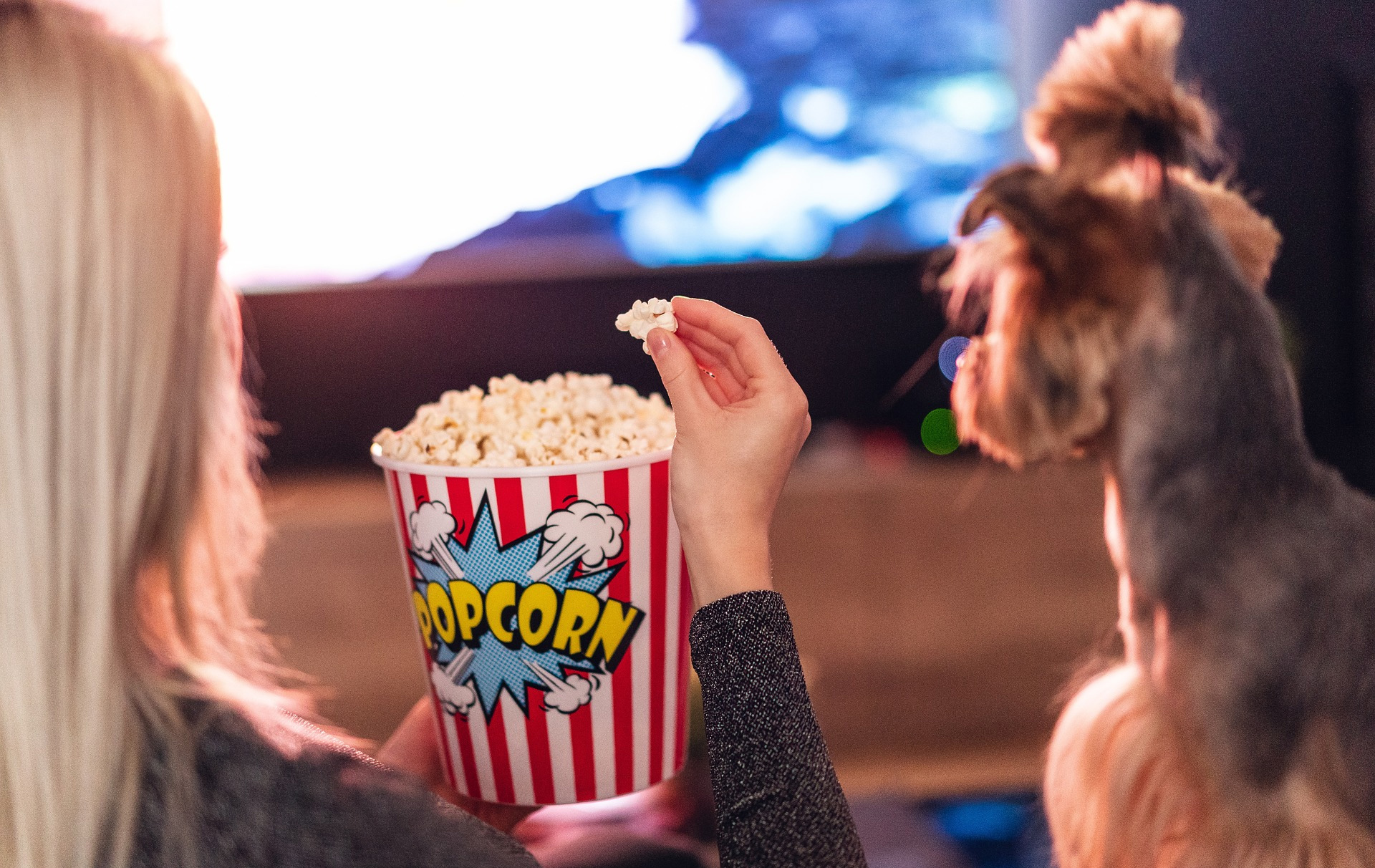 Foto: Frau mit Popcorn von hinten vor einer Leinwand, rechts ein Hund Foto: Frau mit Popcorn von hinten vor einer Leinwand, rechts ein Hund