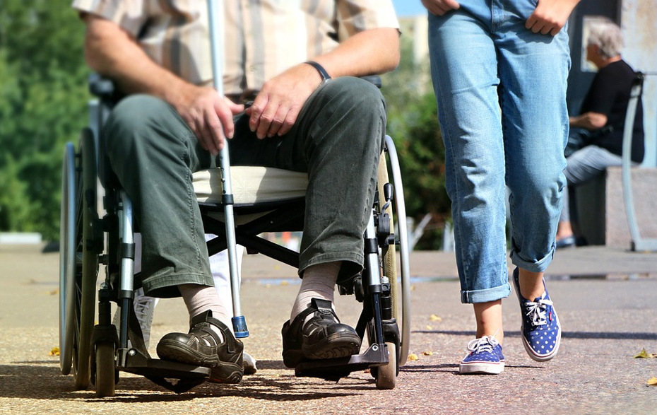 Foto: Senior im Rollstuhl wird von einer jungen Frau begleitet Foto: Senior im Rollstuhl wird von einer jungen Frau begleitet