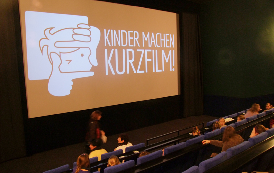 Foto: Kinosaal mit dem „Kinder machen Kurzfilm“-Log auf der Leinwand Foto: Kinosaal mit dem „Kinder machen Kurzfilm“-Log auf der Leinwand