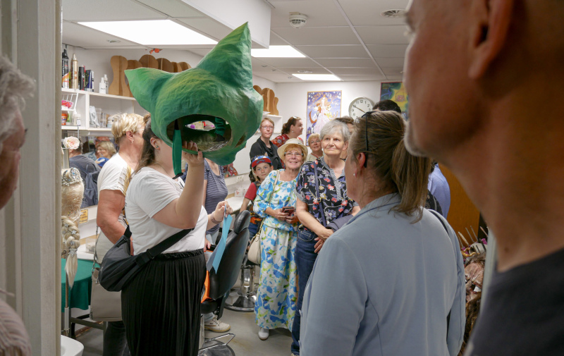 Foto: Frau zeigt mehreren Zuschauern eine grüne Tiermaske Foto: Frau zeigt mehreren Zuschauern eine grüne Tiermaske