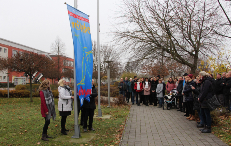 Foto: Die Flagge wird hochgezogen im Beisein zahlreicher Frauen und Männer. Foto: Die Flagge wird hochgezogen im Beisein zahlreicher Frauen und Männer.