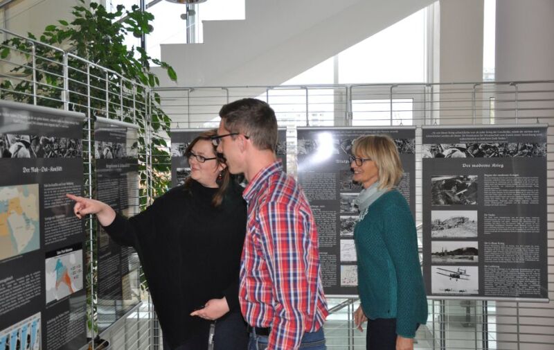 Drei Besucher sehen sich Ausstellungstafeln an. Drei Besucher sehen sich Ausstellungstafeln an.