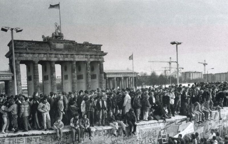 Menschen stehen und sitzen auf der Berliner Mauer Menschen stehen und sitzen auf der Berliner Mauer