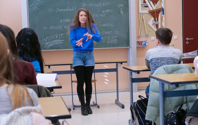 Foto: Schauspielerin steht gestikulierend vor einer Schultafel Foto: Schauspielerin steht gestikulierend vor einer Schultafel