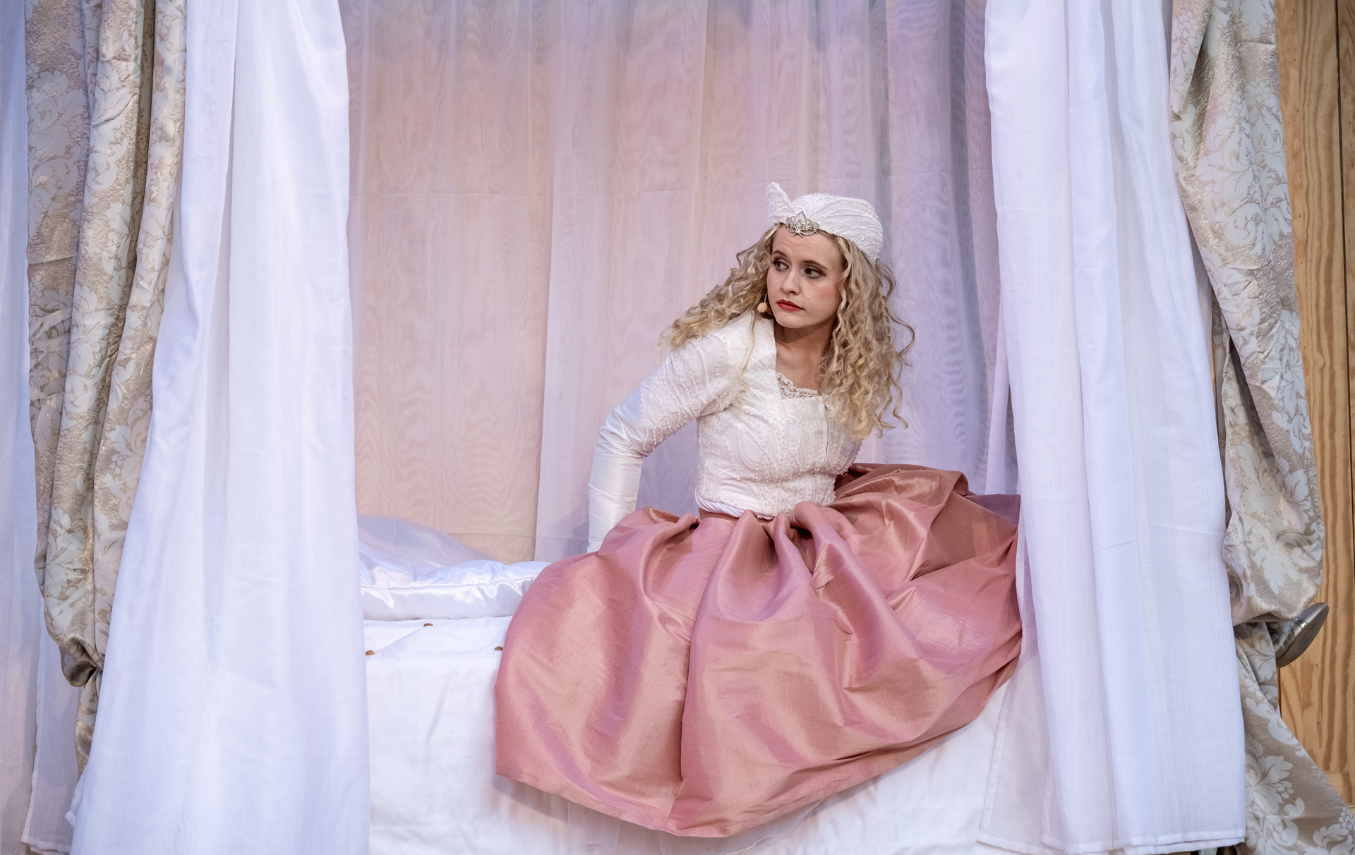 Foto: Schauspielerin in rosa Kostüm sitzt auf einem Bett Foto: Schauspielerin in rosa Kostüm sitzt auf einem Bett